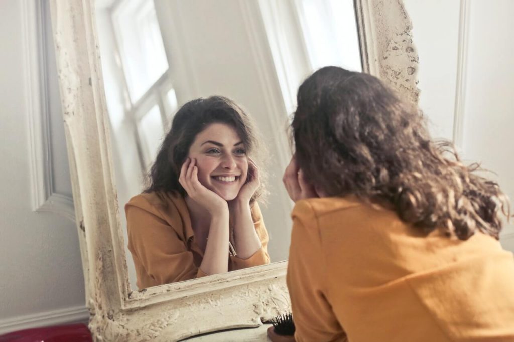 Rozpromieniona kobieta patrzy na swoje odbicie w lustrze